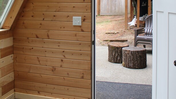 A wooden interior with a sloped ceiling, a door leading outside, and a visible outdoor area with a wooden fence and tree stumps. - Bandon Country Club (Bandon)
