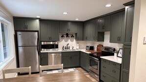A modern kitchen with dark green cabinets, stainless steel appliances, and a wooden dining table. - Bandon Country Club (Bandon)