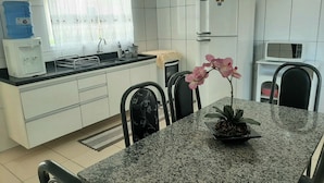 Una cocina con armarios blancos, encimera de granito, pileta, dispensador de agua, refrigerador, microondas y una mesa de comedor con sillas.