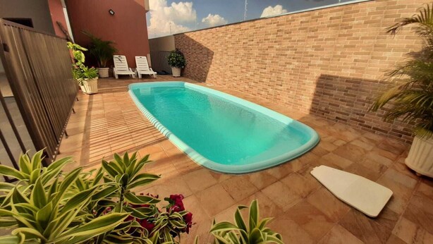 Una piscina rectangular con un borde de baldosas, rodeada de plantas en macetas y un muro de ladrillo.