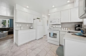 A modern kitchen with white cabinets, a refrigerator, an oven, a microwave, and a coffee maker.