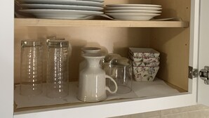 Ein Küchenschrank mit Regalen, auf denen weiße Teller, Schüsseln und eine Kanne stehen.