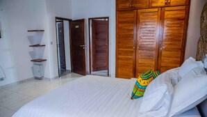 A bedroom with a large bed, wooden wardrobe, and a small shelf unit.