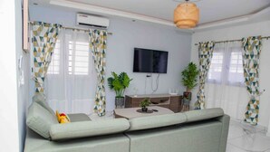 A modern living room with a sectional sofa, a flat-screen TV, and two potted plants.
