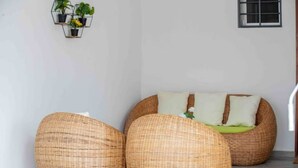 A room with a wicker sofa and two large bean bags, a small wall-mounted plant shelf, and a window.