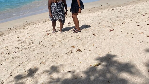 A beach with two people standing on the sand, a clear sky, and distant mountains.
