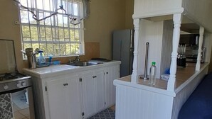 A compact kitchen with a gas stove, a refrigerator, a sink, and a window with curtains.