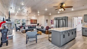 A spacious living area with a large sofa, coffee table, and a fireplace. There is a kitchen with grey cabinets and a stainless steel refrigerator. - Brand New Near PF~Royal Ridge~Indoor Pool-Racing Games (Sevierville)