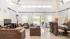 A spacious living room with a television, wicker furniture, and a view of the outdoors.