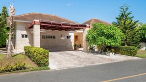 A two-story house with a covered driveway, a palm tree, and various shrubs.
