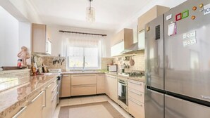 A modern kitchen with stainless steel appliances, a large refrigerator, and a window with a curtain.