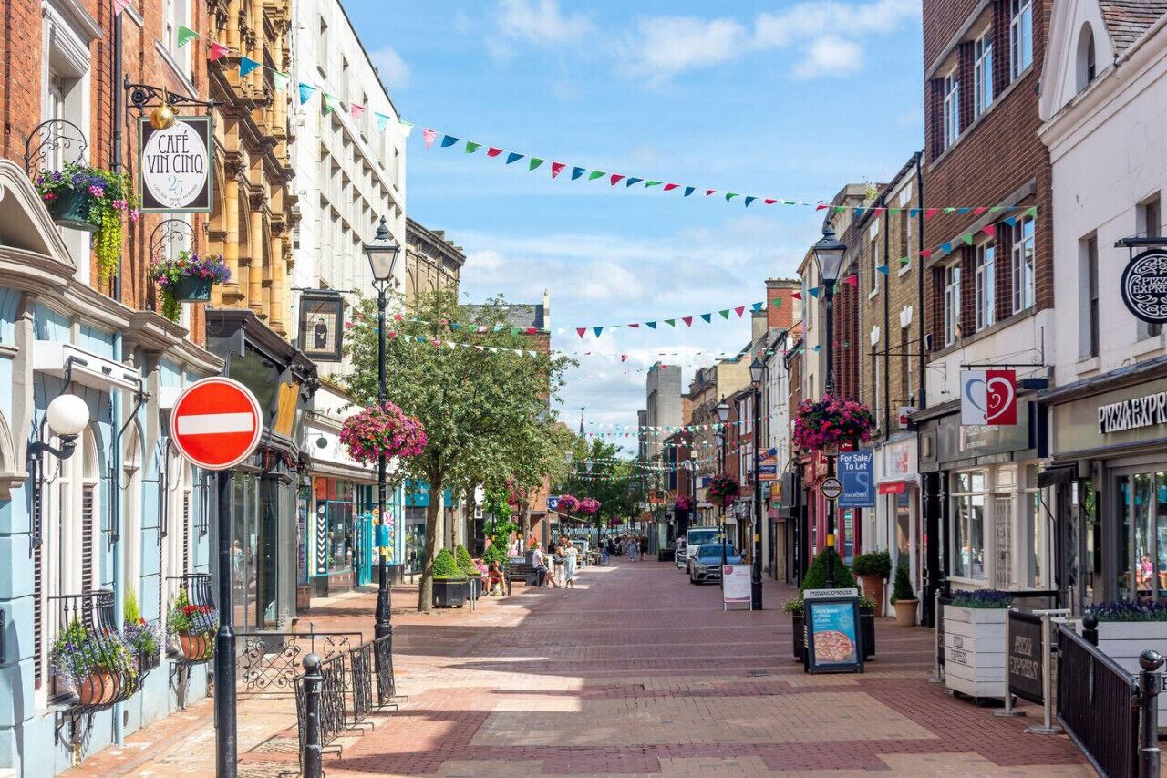 A street lined with shops and a café with outdoor seating, a no entry sign, and colorful flags.