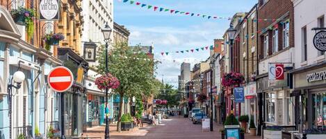 A street lined with shops and a café with outdoor seating, a no entry sign, and colorful flags.