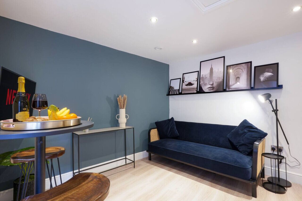 Una sala de estar moderna con un sofá azul oscuro, una mesita con una botella y vasos, y cuadros en la pared.