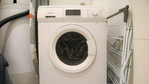 A front-loading washing machine with a digital display, control panel, and a metal drying rack to its right.