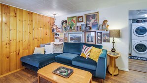 A cozy living room with a blue sofa, wooden coffee table, and a wall decorated with framed pictures and a lamp. - Newport Cabin on Diamond Lake w/ Private Boat Dock (Newport)
