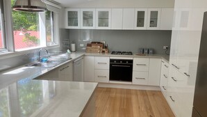 A modern kitchen with white cabinetry, a built-in oven, and a large island with a sink. - Historic Cottage 4 Riverside Dve. Pet friendly, flat fenced yard  on the River. (Warburton)
