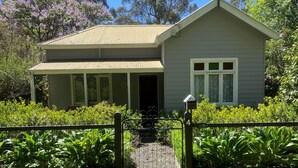 A two-story house with a porch, surrounded by lush greenery and a fenced yard. - Historic Cottage 4 Riverside Dve. Pet friendly, flat fenced yard  on the River. (Warburton)