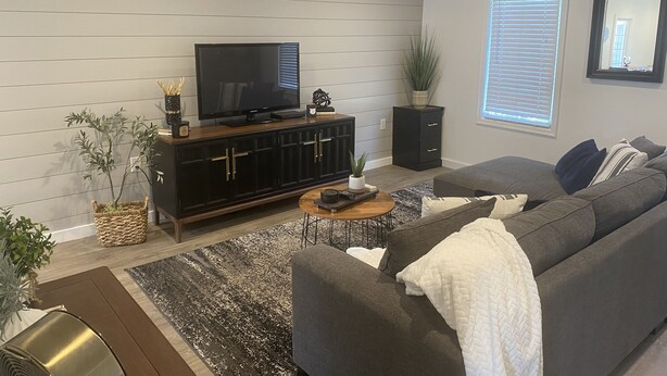 En moderne stue med et fladskærms-tv, en mørk træ-tv-møbel, en grå sofa og en loftventilator.