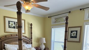 Un lit à baldaquin avec une tête de lit en bois, un ventilateur de plafond et une table de chevet avec une lampe.