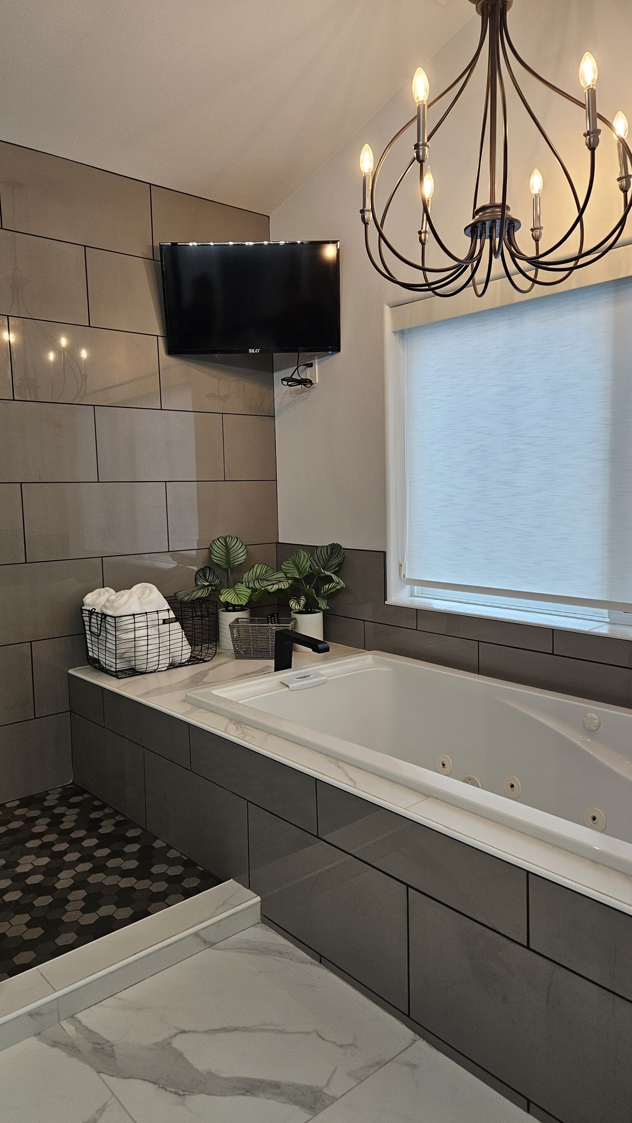 Un bagno moderno con una vasca da bagno ampia, un televisore a parete e un lampadario.