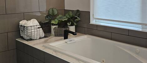 Un bagno moderno con una vasca da bagno ampia, un televisore a parete e un lampadario.