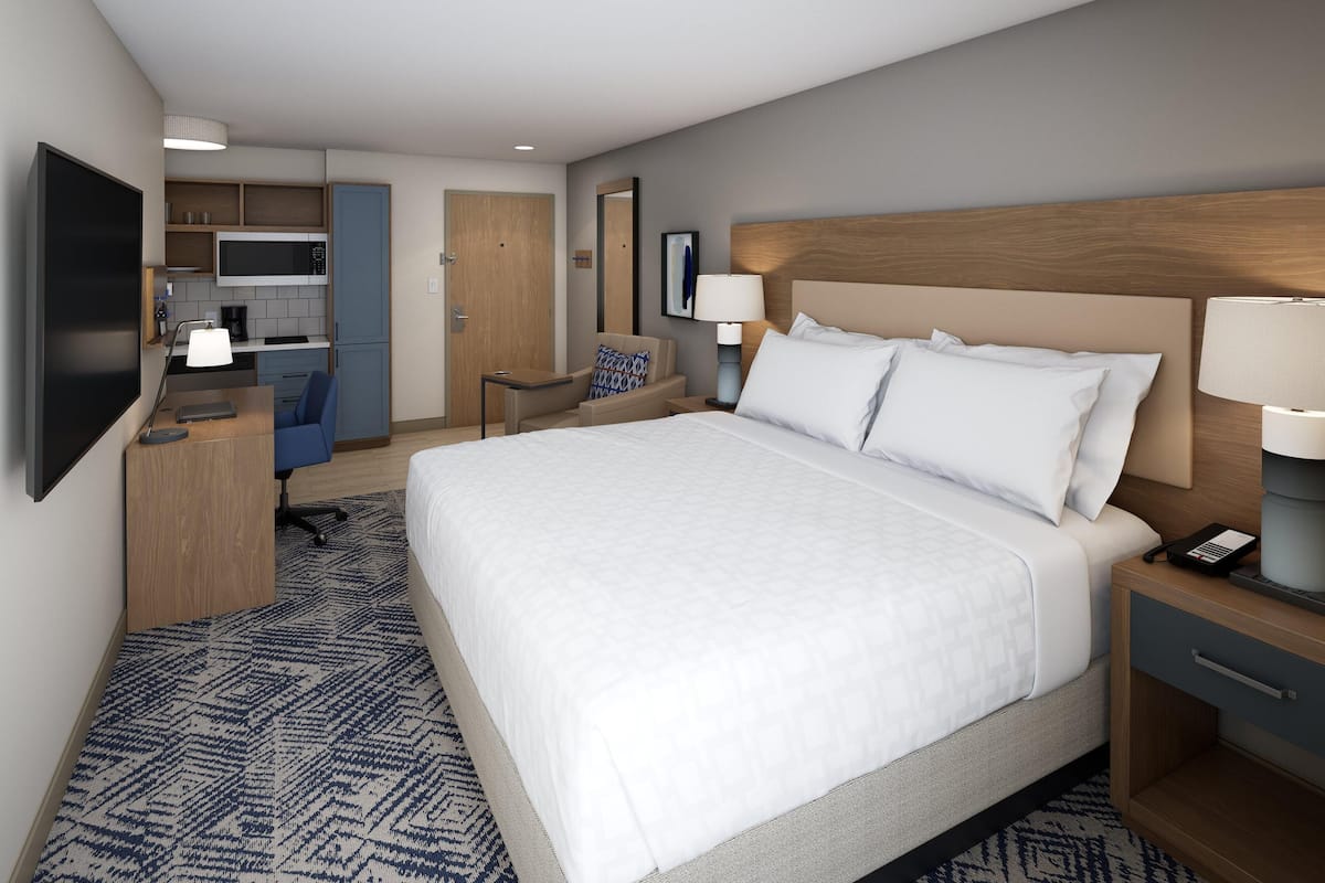 Een hotelkamer met een groot bed, een bureau, een stoel, een magnetron, een koffiezetapparaat en een televisie.