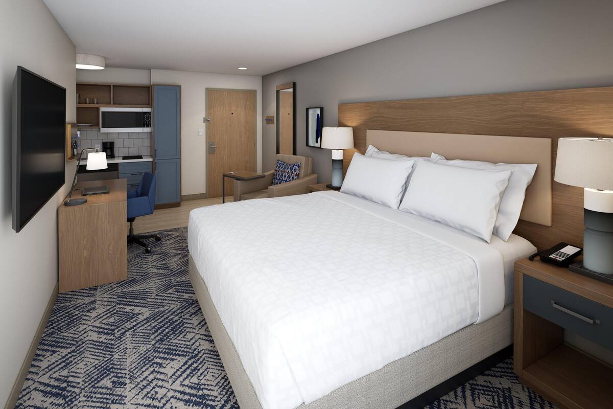 Ein Hotelzimmer mit einem großen Bett, einem Schreibtisch mit Stuhl, einer Küchenzeile und einem Fernseher.