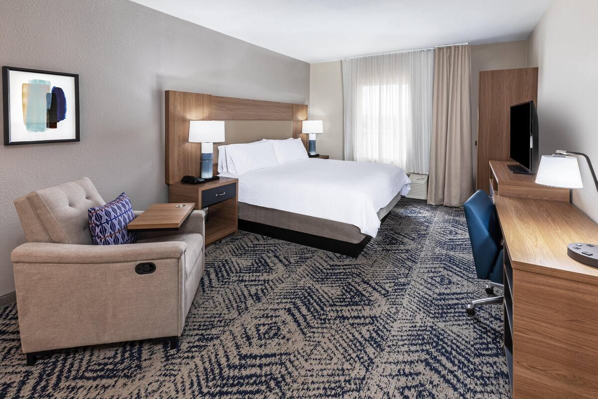 Ein Hotelzimmer mit Bett, Schreibtisch, Sessel, Sofa und Fernseher.