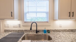 Una cocina con encimera de granito, pileta de acero inoxidable y muebles blancos.