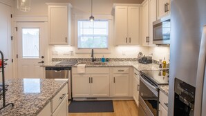 Una cocina moderna con armarios blancos, encimeras de granito, un refrigerador de acero inoxidable y un horno empotrado.
