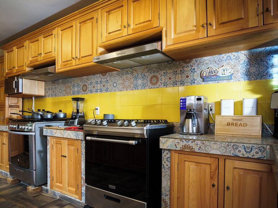 Una cocina con gabinetes de madera, una campana de acero inoxidable, una estufa y una cafetera.