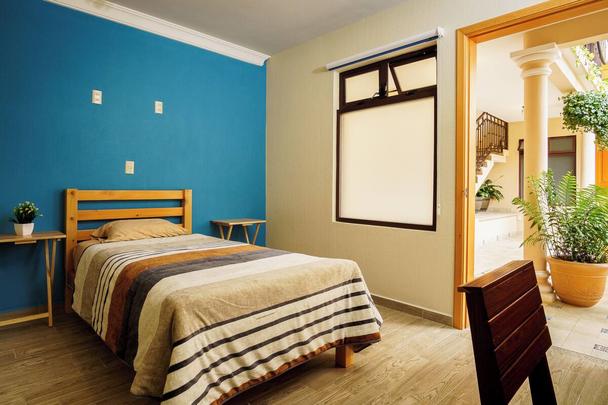 Une chambre à coucher avec un lit, une table de chevet en bois, une plante en pot et une vue sur un escalier.
