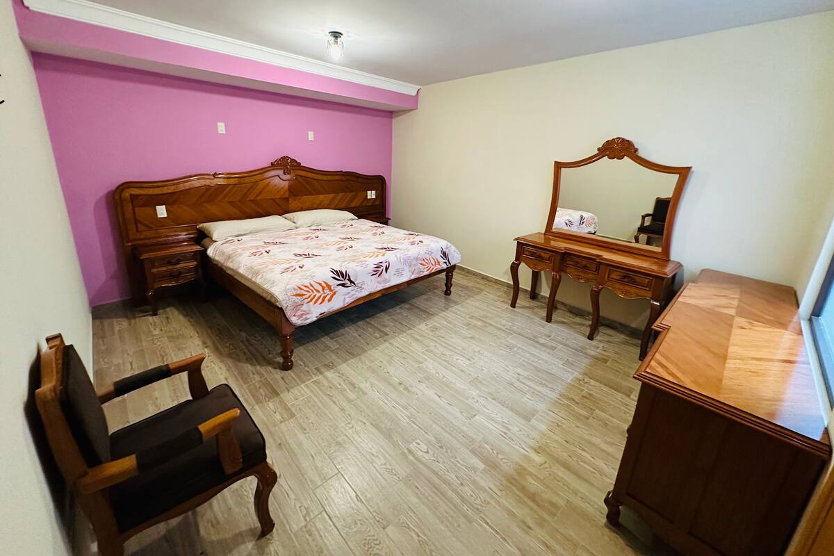 Une chambre à coucher avec un lit en bois, une commode, une chaise et un miroir.