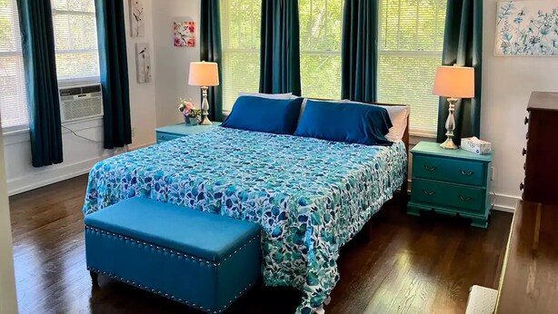 A bedroom with a bed, two nightstands, a bench, and a ceiling fan. - Upstairs @ Courthouse Square - Quirky (Hot Springs)