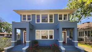 A two-story house with a flat roof, a central entrance, and a small front yard with red flowers. - Upstairs @ Courthouse Square - Quirky (Hot Springs)