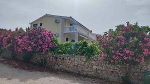 A two-story building with a balcony, surrounded by pink flowering bushes and a stone wall. - Holiday apartment Rubi 3, a beautiful apartment with an enchanting view of the sea (Primošten)