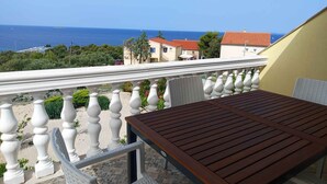 A balcony with a wooden table and white balustrades overlooking a coastal area with buildings and the sea. - Holiday apartment Rubi 3, a beautiful apartment with an enchanting view of the sea (Primošten)