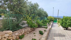Ein Gartenpfad mit Steinmauer und viel Grün, der zum Blick auf das Meer führt.
