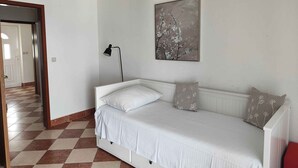 Ein Schlafzimmer mit einem weißen Bett, einer Stehlampe und einem an der Wand hängenden Kunstwerk.