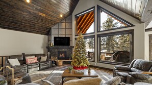 Ein geräumiges Wohnzimmer mit Kamin, Ledersofas, einem Weihnachtsbaum und großen Fenstern mit Blick ins Freie.