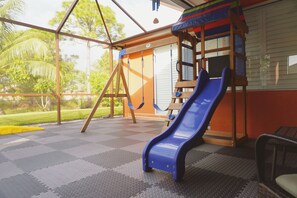 A covered outdoor play area with a slide, a swing set, and a climbing structure. - Home Feel with a Vacation Ambience (Port St. Lucie)