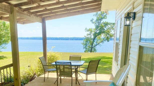 A covered patio with a table and chairs, overlooking a lake.