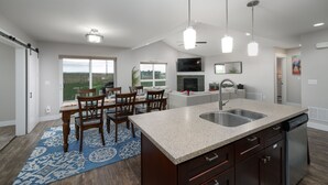 A modern kitchen with a large island, a dining area with a blue patterned rug, and a view of the outdoors through large windows. - Mountain Views, Single family home near airport. Skyview Retreat! (Belgrade)
