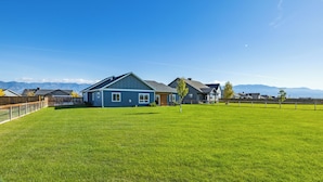 A residential property with a large grassy yard, a blue house, and mountains in the background. - Mountain Views, Single family home near airport. Skyview Retreat! (Belgrade)