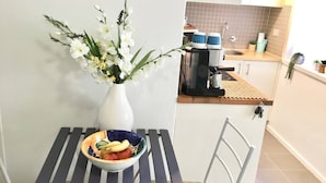 Una cocina con un jarrón blanco lleno de flores, un frutero y una cafetera sobre la encimera.