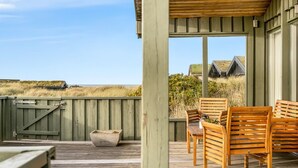 Una terraza de madera con una zona de estar cubierta, una jardinera de hormigón y vistas del paisaje circundante.