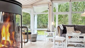 Een gezellige woonkamer met een open haard, grote ramen en een comfortabele zithoek.