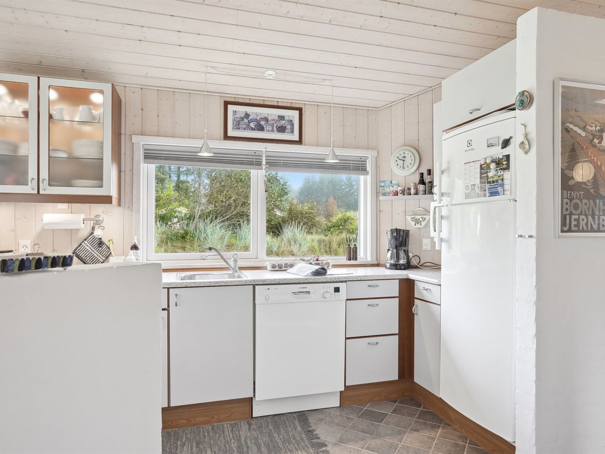 Una cocina moderna con armarios blancos, lavavajillas integrado, un ventanal grande y un refrigerador con imanes.
