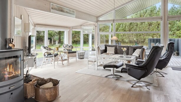Een ruime woonkamer met een open haard, comfortabele zithoek en grote ramen met uitzicht op de omgeving.
